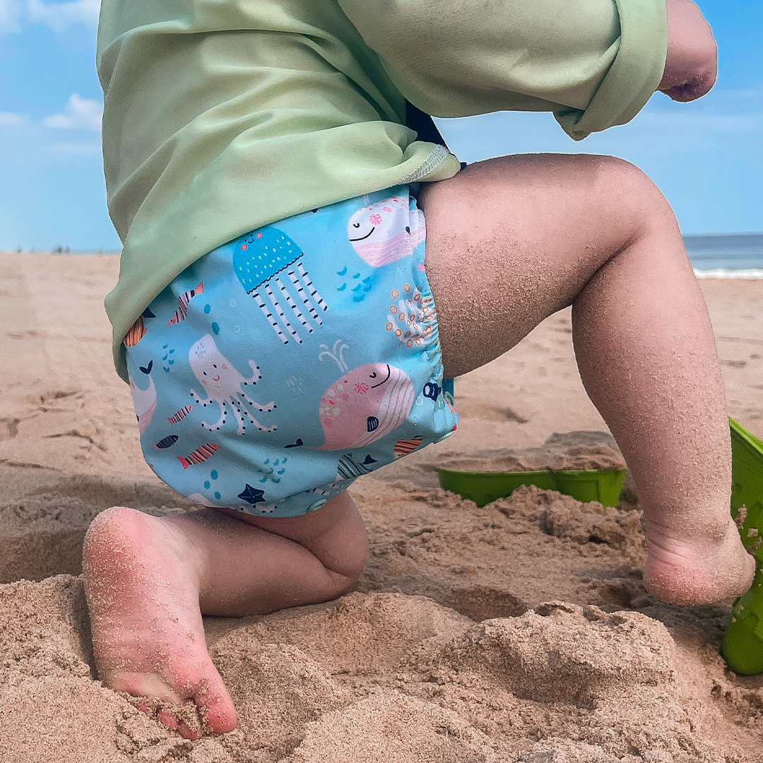 Pocket Diaper being used as a swim diaper for the beach. Featuring art by Marina Solodka with jelly fish and ocean animals.