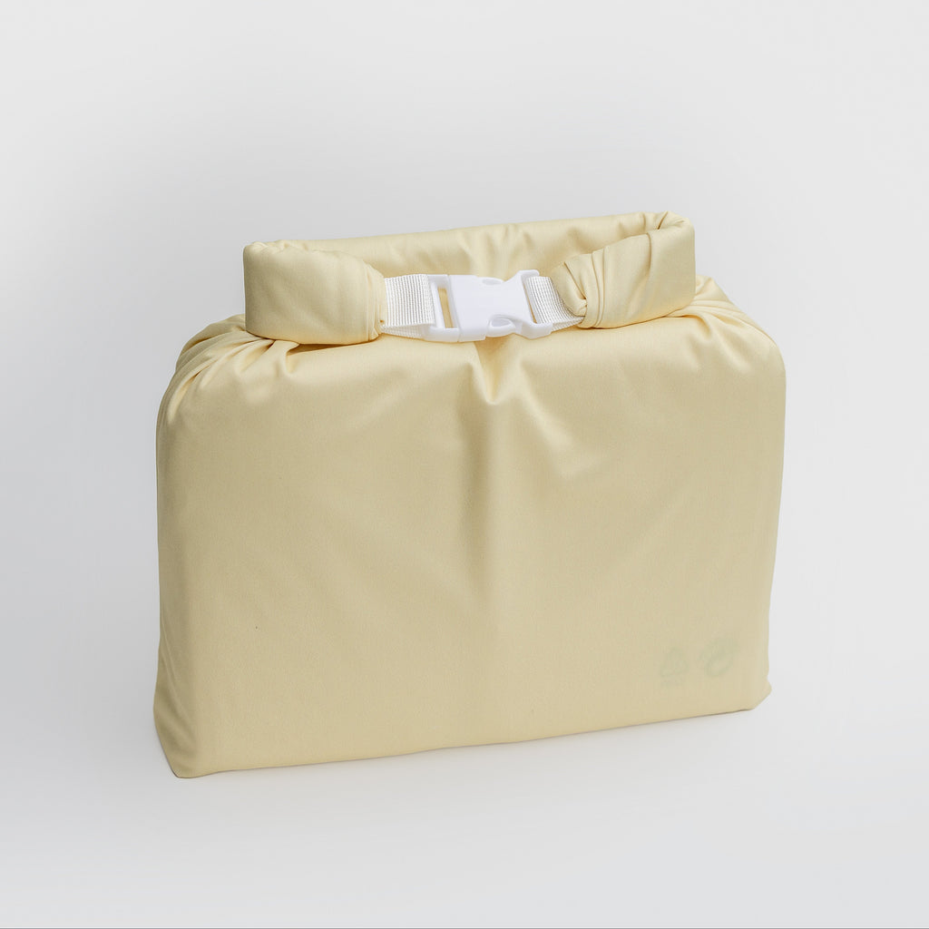 A pale yellow waterproof dry bag with a roll-top closure and white plastic buckle, shown on a clean light gray background.