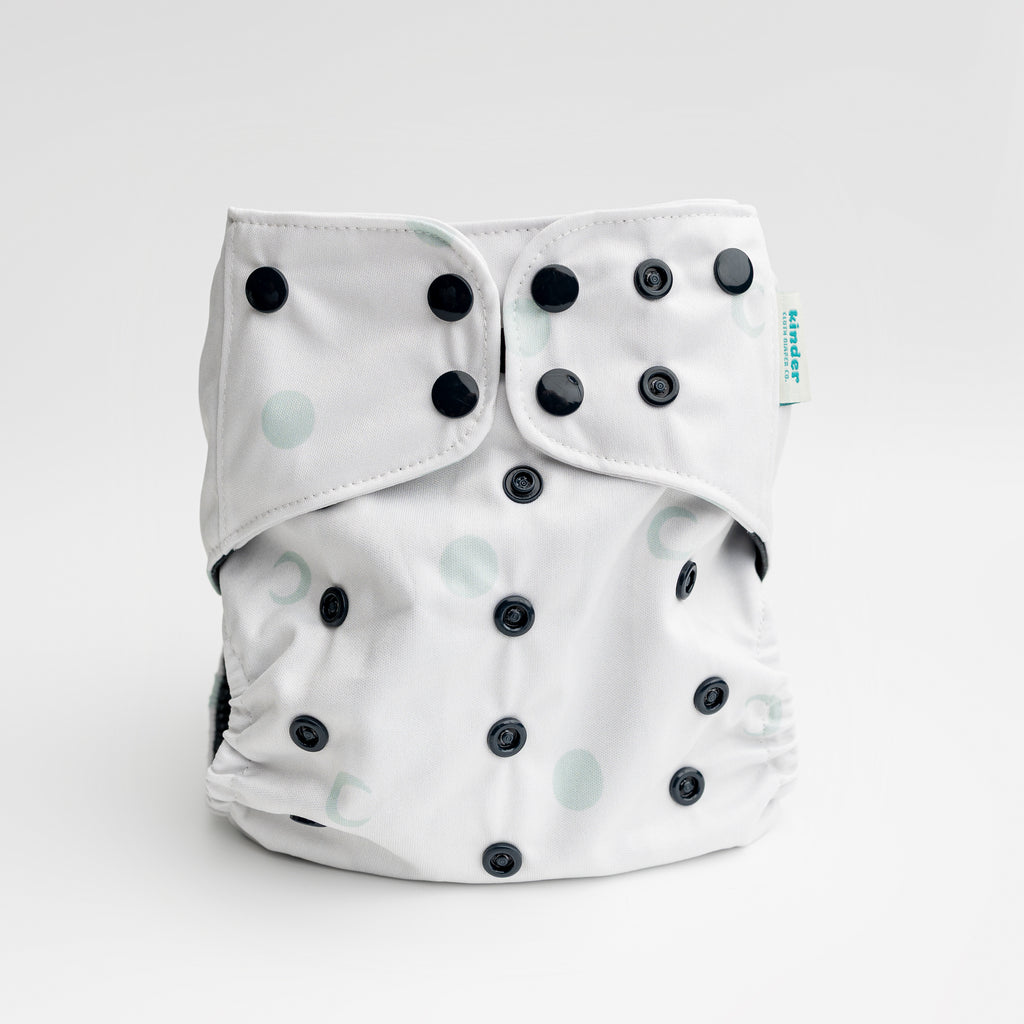 white cloth diaper with green moons and black snaps by kinder cloth diaper co with art by Malika Buttinger, one size fits most