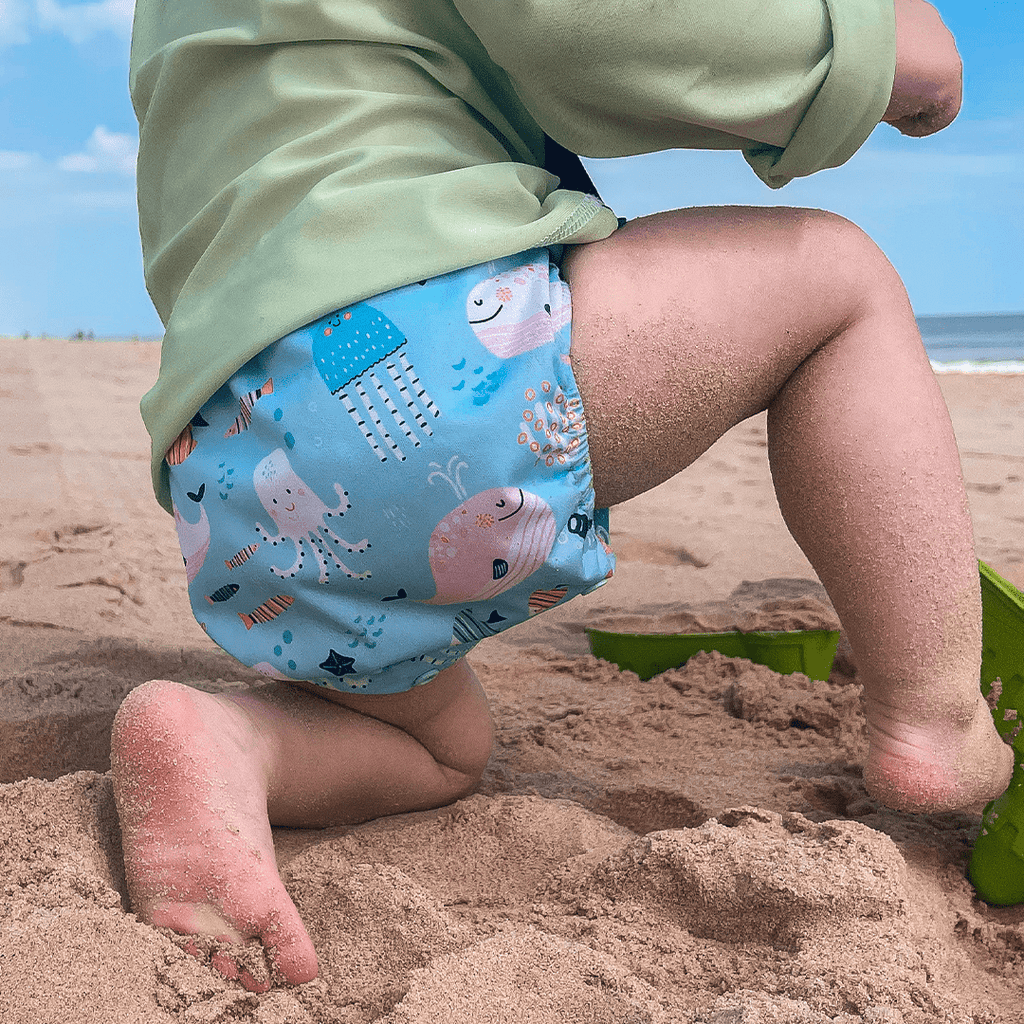Pocket Diaper being used as a swim diaper for the beach. Featuring art by Marina Solodka with jelly fish and ocean animals.