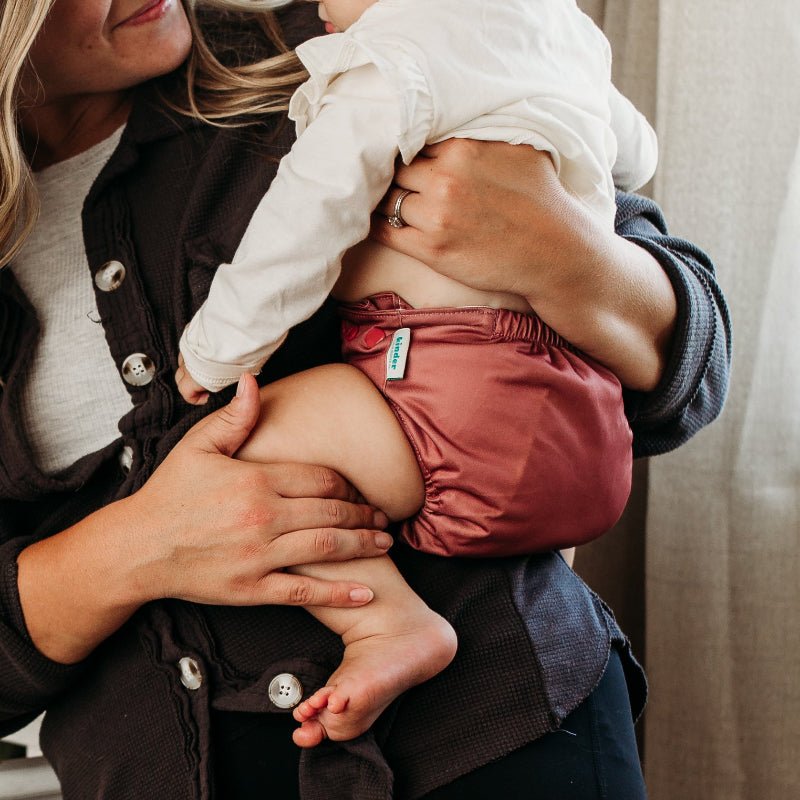Woman holding a baby wearing a pink cloth diaper with a visible Kinder Cloth diaper Co label.