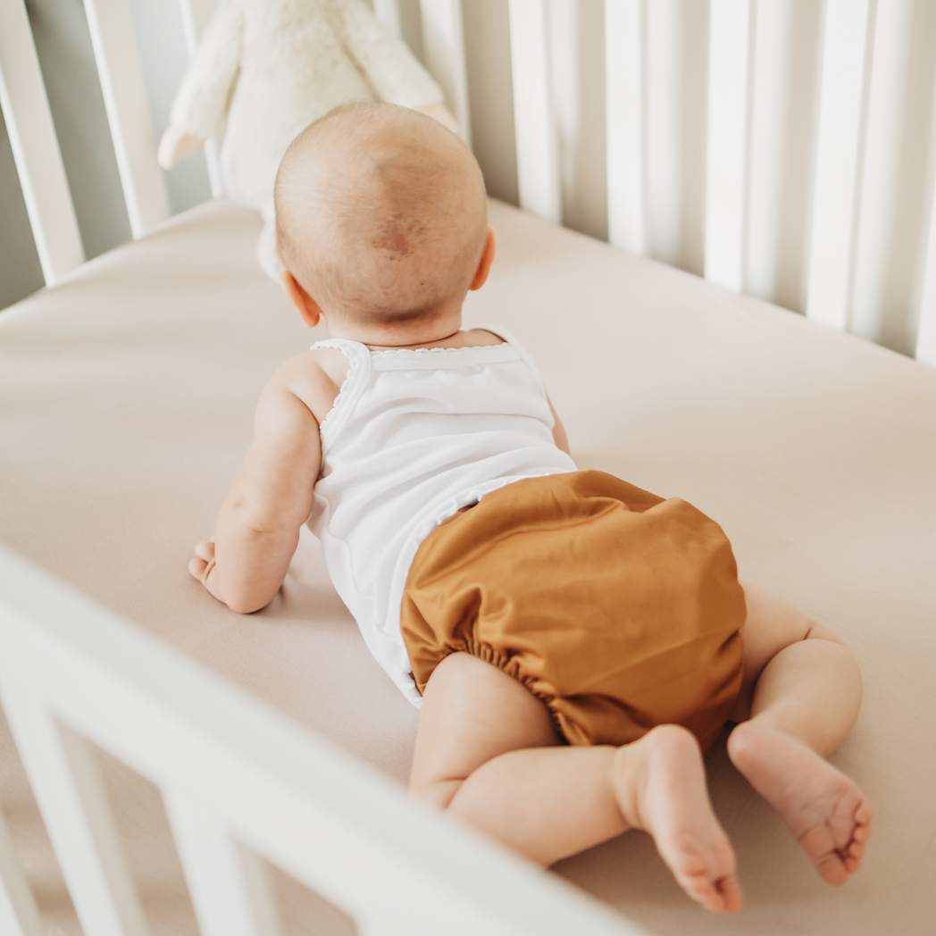 Baby wearing reusable modern cloth diaper in a burnt orange color in crib ecofriendly cloth nappies